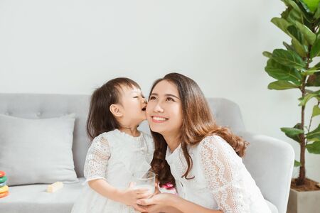 People and family concept - happy smiling girl kissing her mother on sofa at home