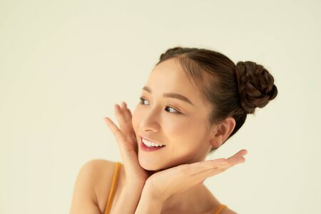 Close-up portrait of adorable Asian girl with buns touching checks isolated over light background.の写真素材