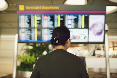 Passenger traveling at the flight information board in airport terminal waiting hall area checking...