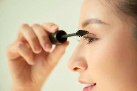 Portrait of young Asian woman applying mascara over light background.の写真素材