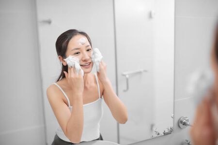 Beautiful young woman washing her face foam in a bathroom.の写真素材