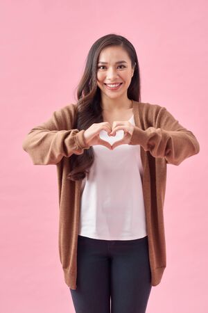 Asian woman making a heart shape with her hands, isolated over pink backgroundの写真素材