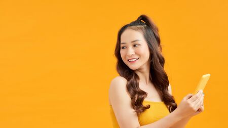 Happy young Asian woman using smartphone over orange background.の写真素材