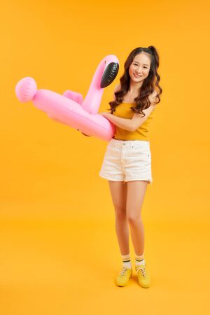 Happy young Asian woman dress casual clothes posing with inflatable flamingo over orange background.の写真素材