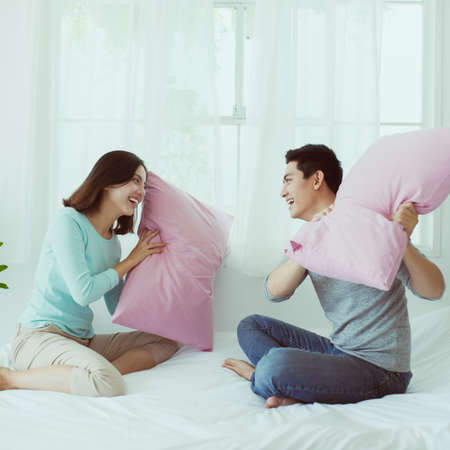 Young happy couple beat the pillows on the bed in a bedroom at home.