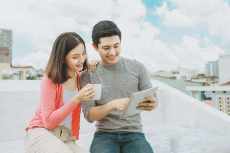 Young Asian couple using tablet and drinking tea/coffee together on rooftop.の写真素材
