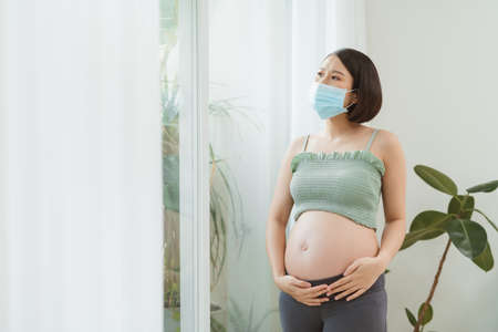 Young pregnant asian woman in medical mask stay alone at home for self quarantineの写真素材