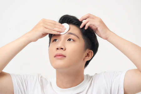 Beauty portrait of a handsome man standing isolated over white background, using cotton padの写真素材