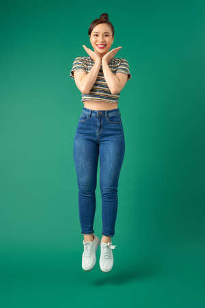 Happy carefree young woman jumping isolated over green background.の写真素材