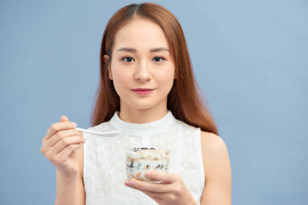Beautiful young woman eating fresh yoghurt, raisins and oatmeal for breakfast.