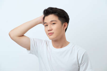 Condifent young asian man with stylish haircut and appealing eyes, touching dark hair, posing against white backgroundの写真素材