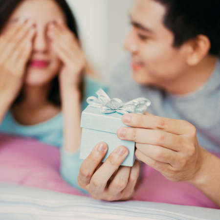 Handsome elegant guy is presenting a gift card and box to his beautiful girlfriend and smilingの写真素材