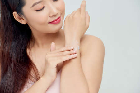 Smiling young woman applies cream on her hands. On a white background.の写真素材