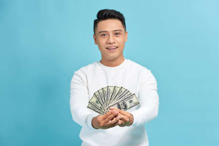 Attractive asian man holding a fan of hundred dollar bills over white background.の写真素材