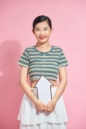 Beautiful young girl standing isolated over pink background, pointing with an arrow up at copy spaceの写真素材