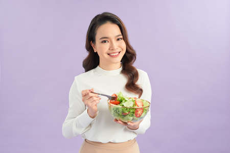 Young asian woman beaming while eating fresh saladの写真素材