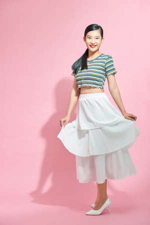 Portrait of happy young beautiful Asian lady in long skirt turning around to face camera, with copy space for advertisementの写真素材