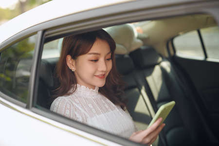 Reading information from smartphone. Smart businesswoman sits at backseat of the luxury car with...