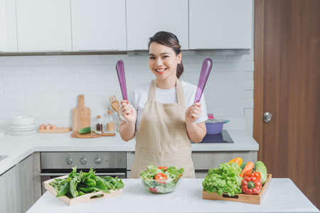 Smiling young woman in apron stand in modern kitchen preparing salad