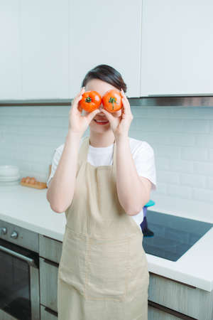 Housewife attractive lady arms holding two big tomato hiding eyes playful mood enjoy morning cookingの写真素材