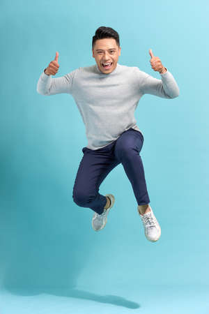 Overjoyed guy jumping and showing thumbs up over blue studio backgroundの写真素材