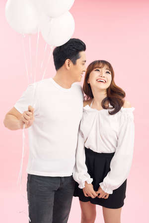 Funky young couple holding balloons while standing against pink backgroundの写真素材