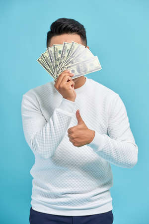 Photo of funny man in casual t-shirt covering his face with fan of money in dollar currency isolated...