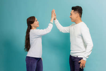 Image of friendly young people man and woman in basic clothing laughing and giving high five isolated over blue backgroundの写真素材