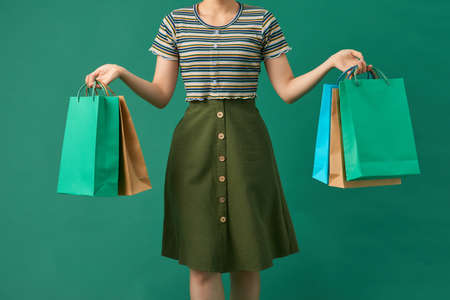 Beautiful young asian woman with colored shopping bags over green background