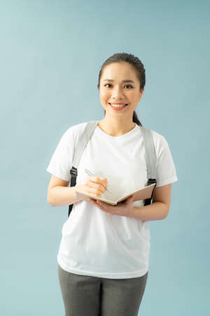 Portrait of a happy friendly girl student with backpack holding books  isolated over blue backgroundの写真素材