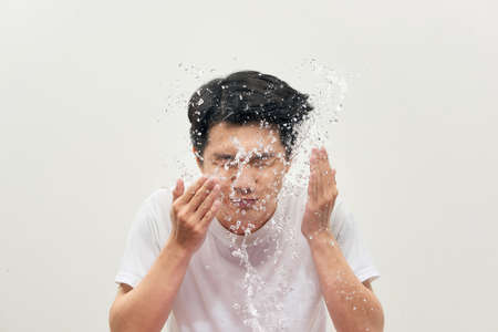 Young man spraying water on his face over white backgroundの写真素材