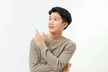 Isolated portrait of happy smiling Asian man pointing hand to empty space aside studio shot white backgroundの写真素材