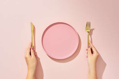 Woman with fork, knife and empty plate on pink background, top viewの写真素材