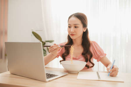 Young asian business woman working and eating asian noodles