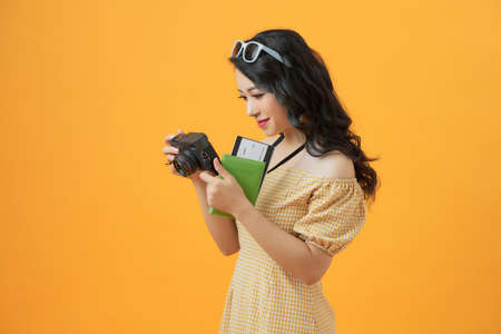 Photo of young tourist lady with camera isolated over yellow background wall holding passport with...