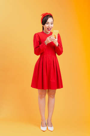 Full length body of surprised young Asian woman reading news while standing over orange background.の写真素材
