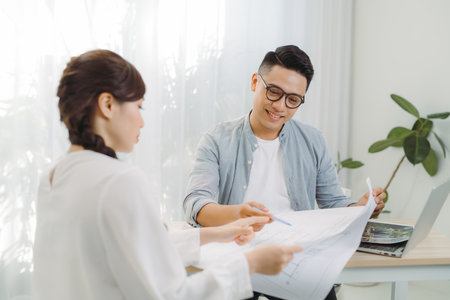 Male and female architect discussing a set of blueprints spread out on a table at office.の写真素材