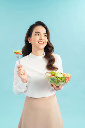Beautiful young asian eating salad with big smile happy beaming face in seamless blue isolated background.の写真素材