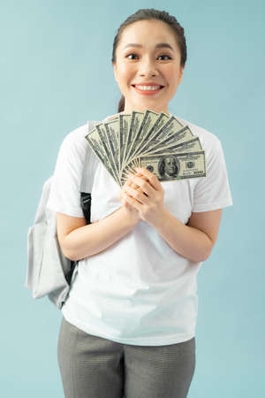 Happy girl student isolated on blue background, hold fan of cash money in dollar banknotes doing...