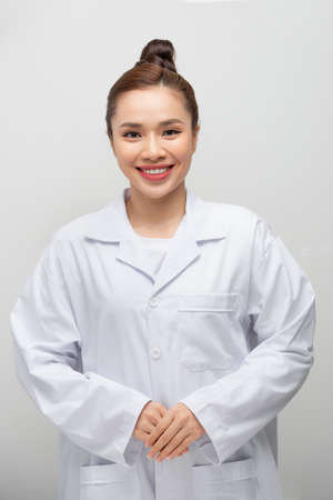 Young asian doctor woman wearing coat standing over isolated white background with a happy and cool...