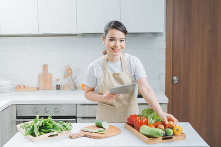 Happy woman looking recipe tablet kitchen reading cookingの写真素材