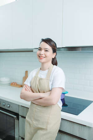 smiling, beautiful woman standing with crossed arms and looking at camera in kitchenの写真素材