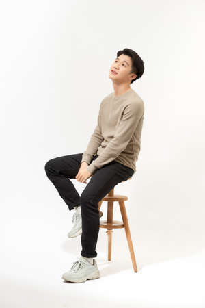 Full body portrait of handsome young Southeast Asian man sitting on high chair,の写真素材
