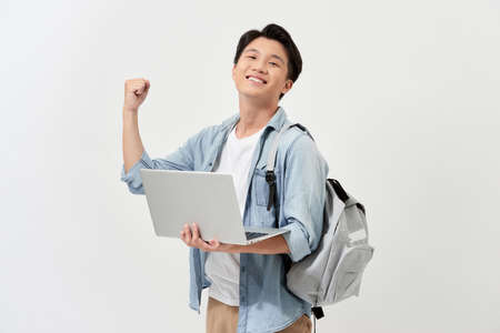 Happy attractive young Asian man holding laptop and backpack over white background.の写真素材