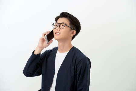 Young Asian man taling on phone while standing over white background.の写真素材