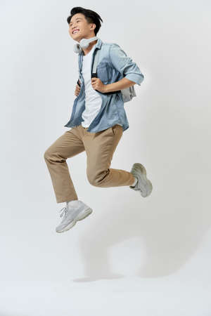 Full length portrait school man with headphone isolated on white running while listening to musicの写真素材