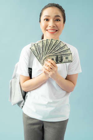 Happy girl student isolated on blue background, hold fan of cash money in dollar banknotes doing winner gestureの写真素材