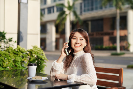 Young and beautiful Asian freelance business woman using a smart phone at the restaurant terrace in the urban cityの写真素材