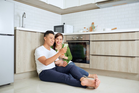 Love is in the air. Beautiful young couple drinking coffee and orange juice while sitting on the kitchen floor at homeのeditorial素材