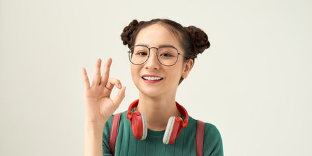 Young lady in eyeglasses holds books and shows ok sign